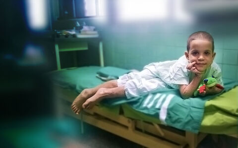 A young Mission Plasticos patient smiling from a hospital bed, holding a stuffed toy