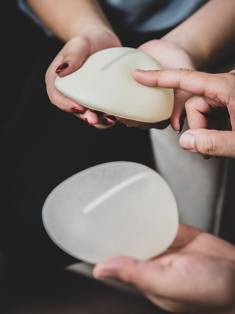 Hands holding two smooth breast implants for comparison